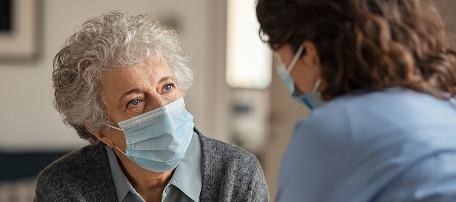 An elderly woman wearing a mask talks to a health care provider.