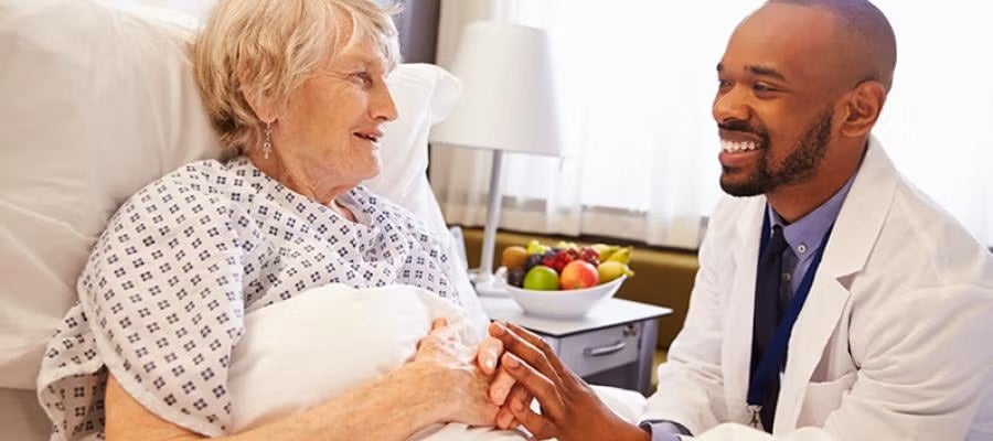 An elderly patient in a hospital bed talks with her physician.