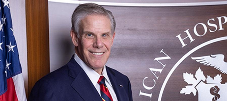 Rick Pollack, president and CEO of the American Hospital Association, standing in front of the AHA seal and a United States flag.