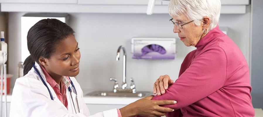 A black female doctor examines the arm of a elderly white woman.